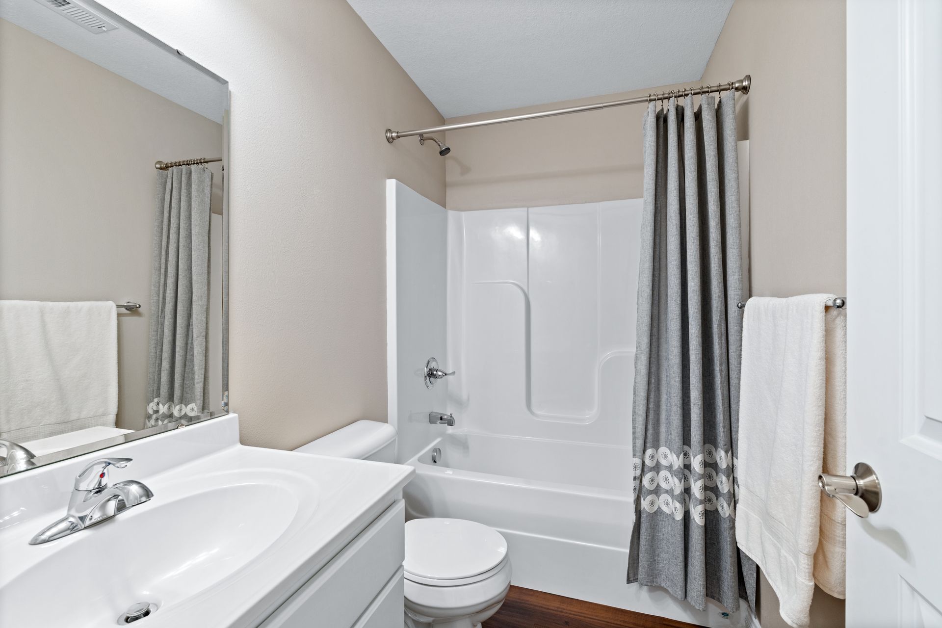 Bathroom with white sink, toilet, tub, gray shower curtain, and beige walls.