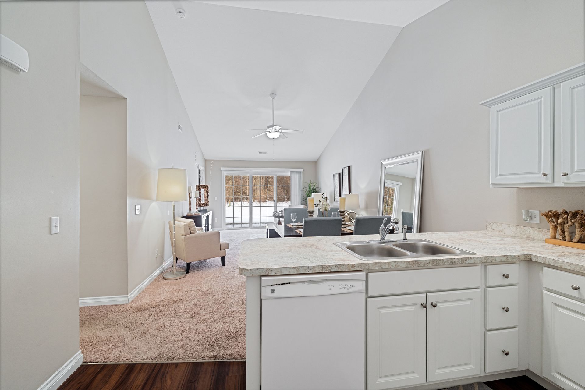 Kitchen with white cabinets and granite countertops, leading into a living and dining area with snowy view.
