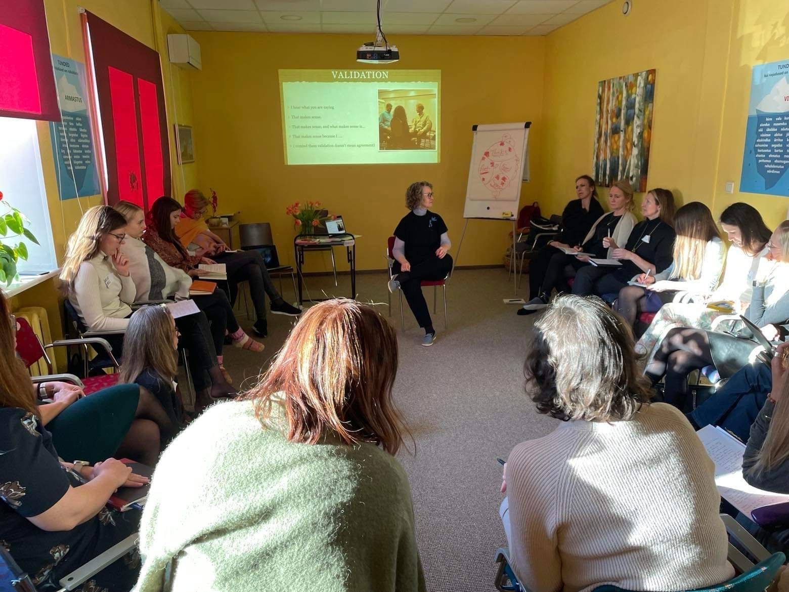 A group of people are sitting in a circle in front of a projector screen.