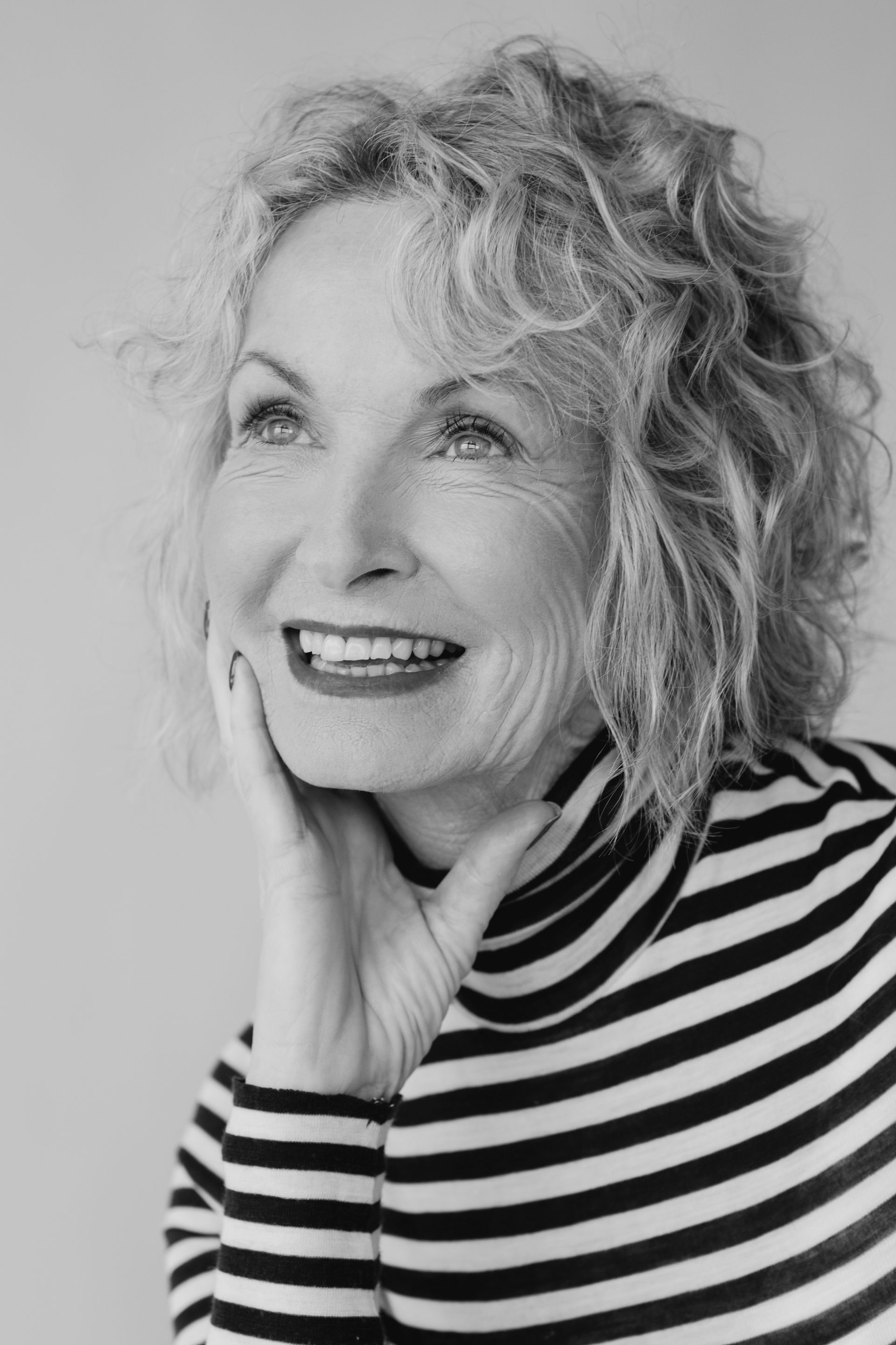 A black and white photo of a woman wearing a striped turtleneck and smiling.