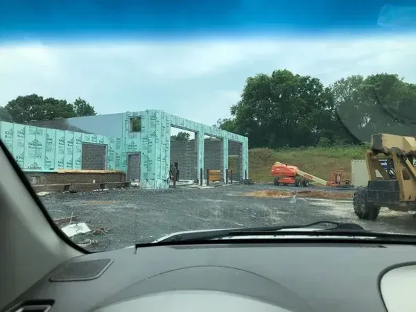 Construction site with a partially built building. Green insulation is visible. A person is standing nearby.