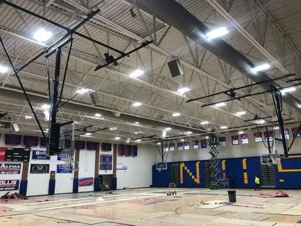 Interior of a gymnasium under construction with basketball hoops, banners, and blue/gold accents.