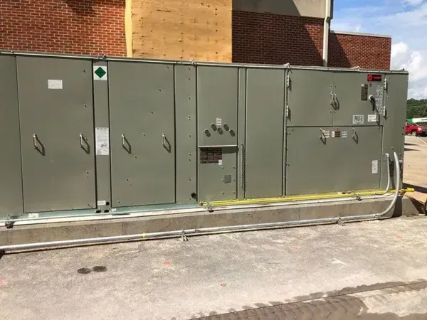 Gray HVAC unit on a concrete base, mounted outdoors near a brick building.