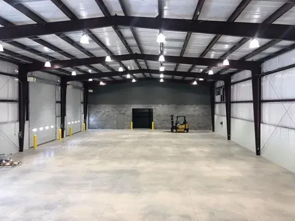 Empty warehouse interior with metal beams, concrete floor, and loading dock. A forklift sits in the center.