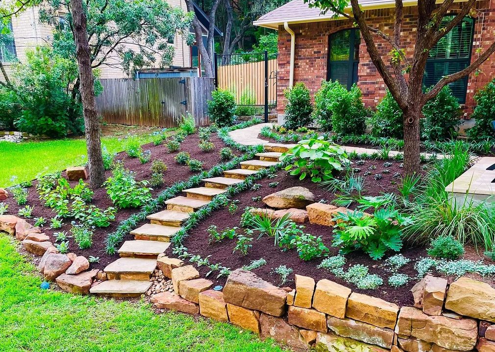 Stone steps in a landscaped garden leading to a small brick shed, with green grass and shrubs.