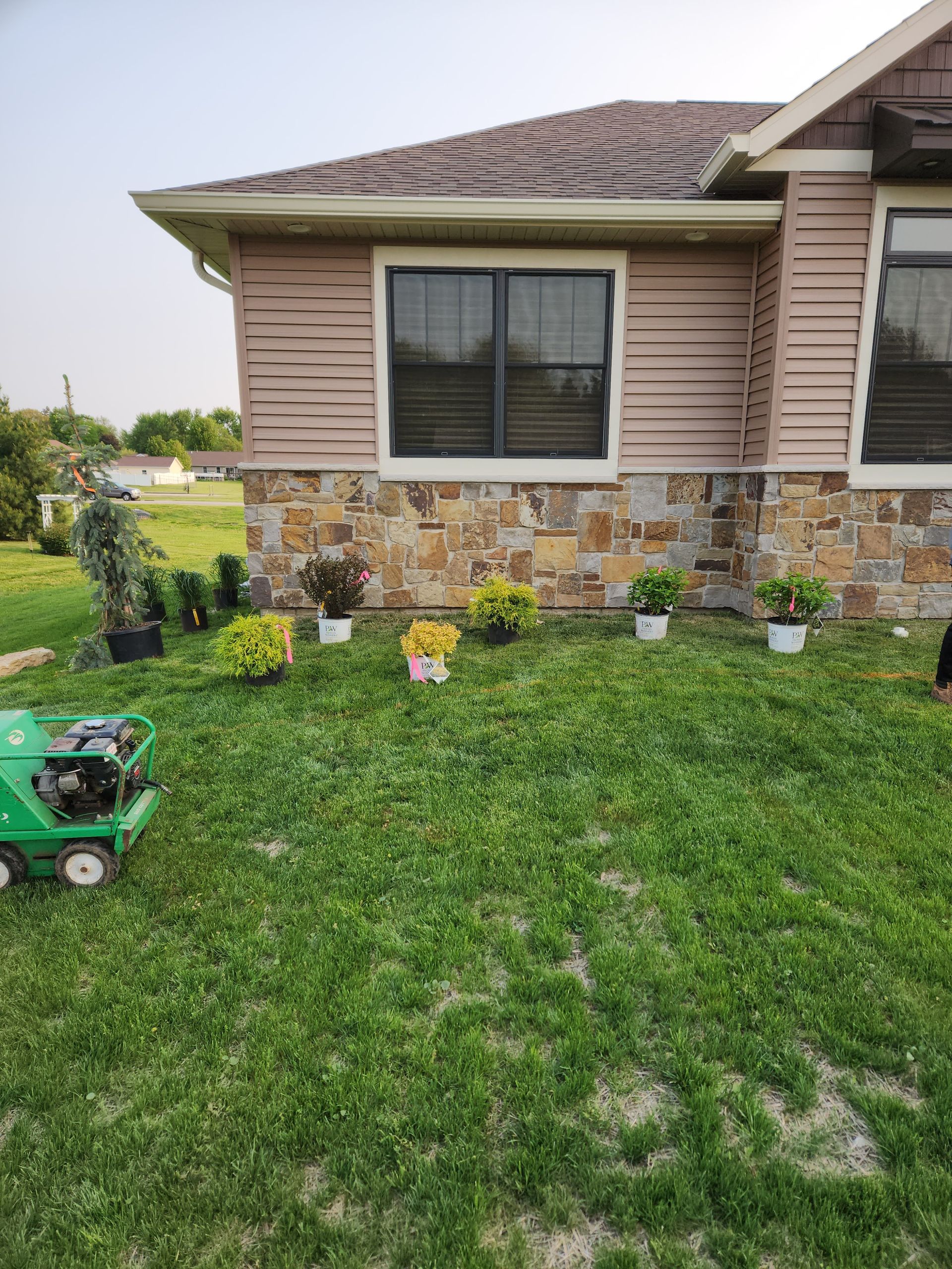 House exterior with tan siding and stone foundation; small potted plants line the lawn.