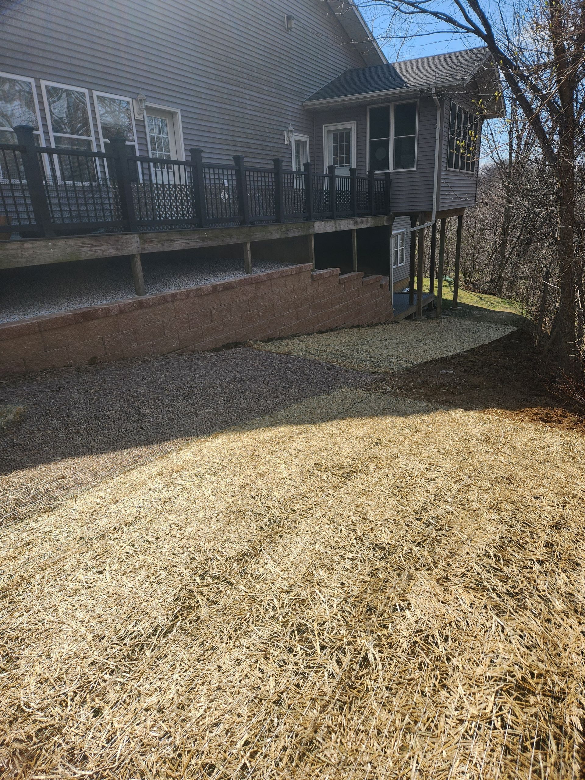 Backyard with a house, deck, retaining wall, and mulch ground covering.
