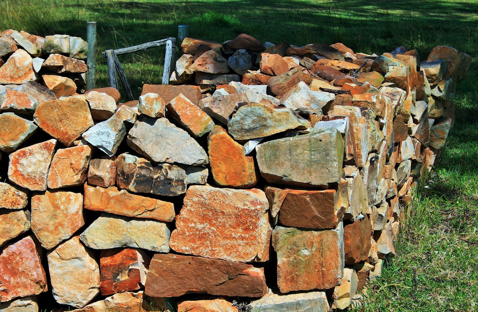 Stone wall made of various colored rocks in a grassy outdoor setting.