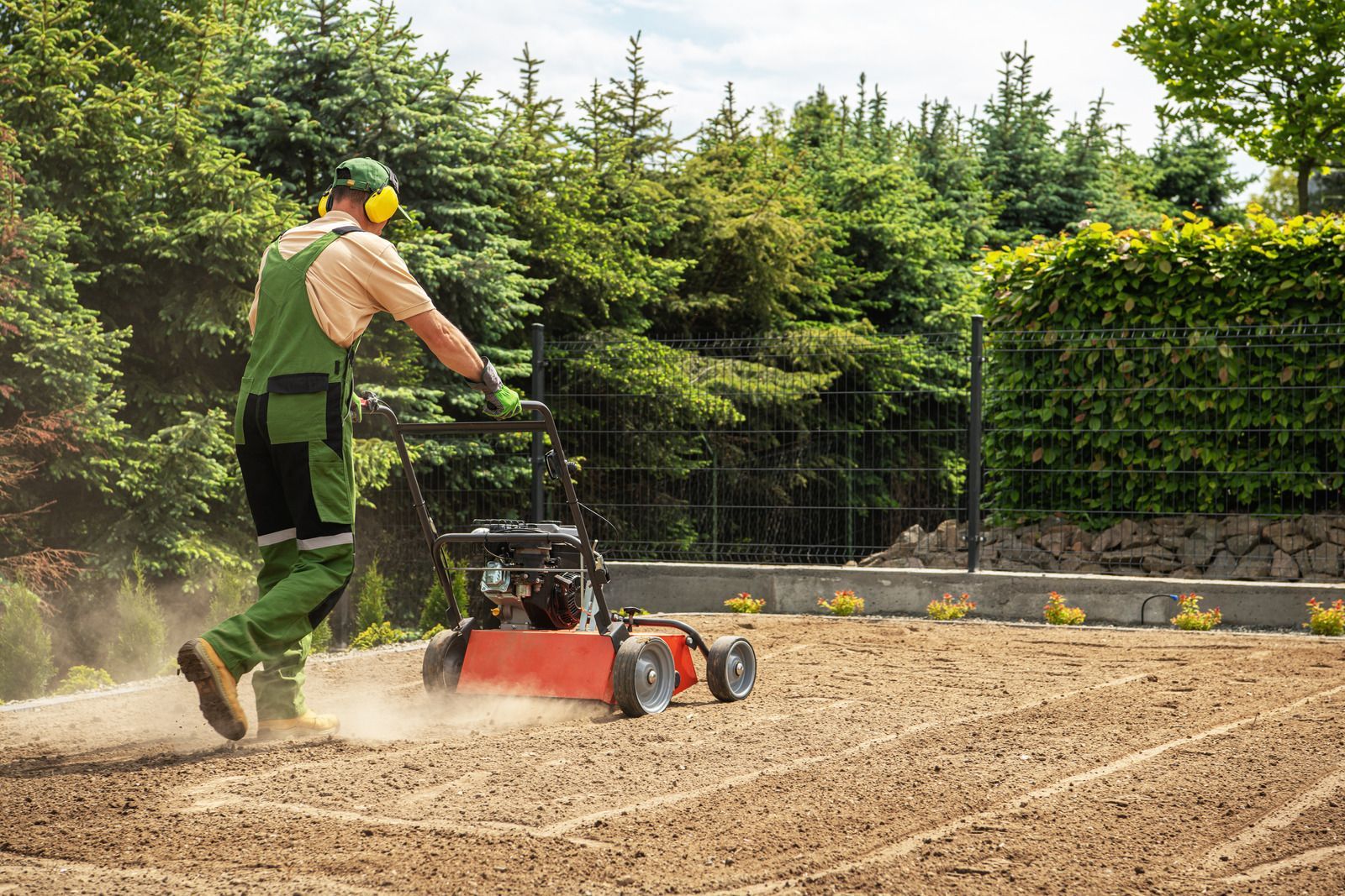 Man using a lawn aerator, preparing soil for planting in a backyard, with trees in background.