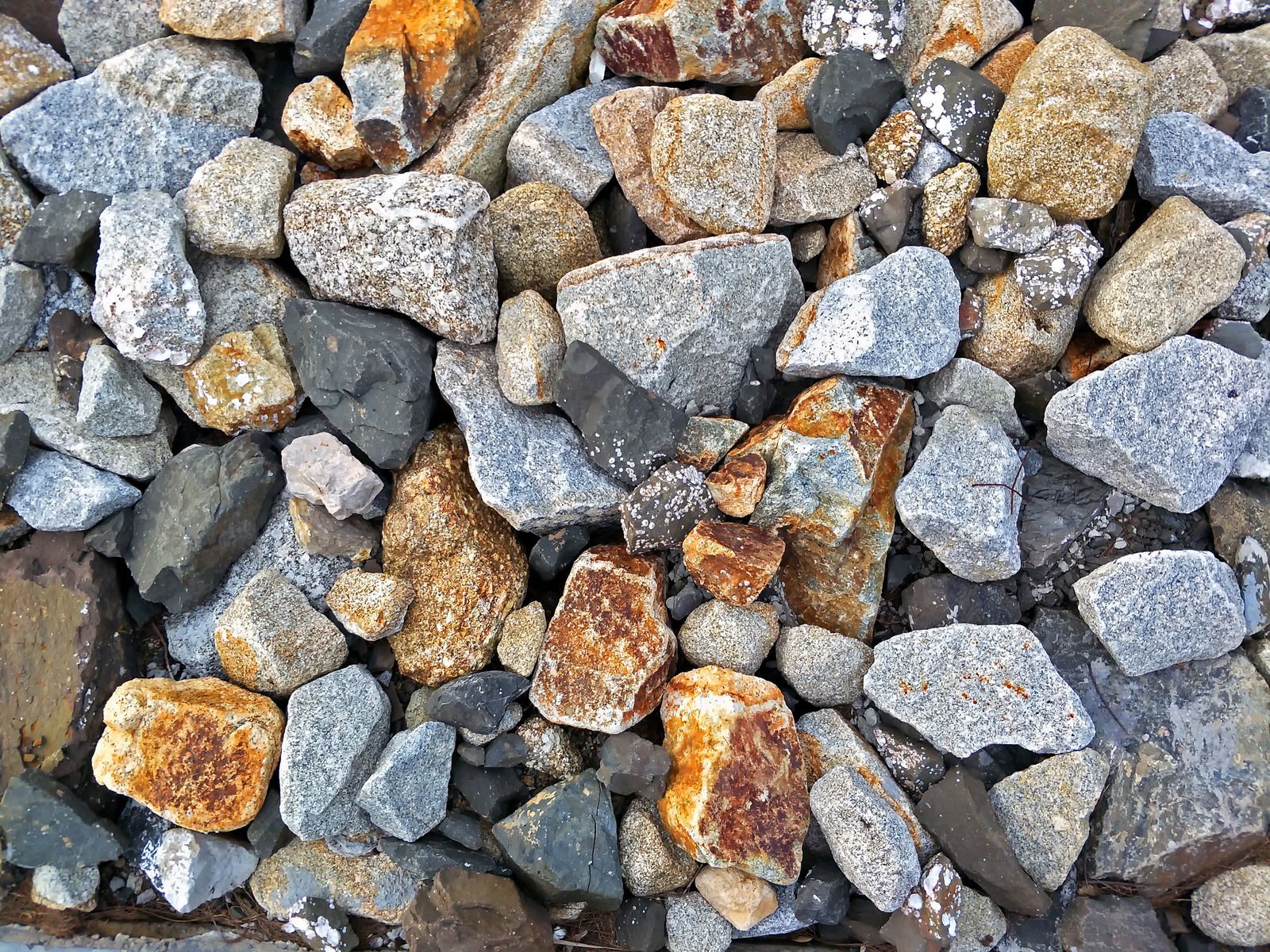 Pile of mixed-color rocks: gray, orange-brown, and black, scattered in a close-up view.