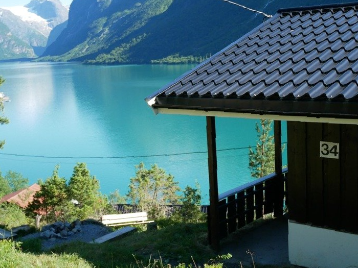 Innsjø og fjell sett fra en veranda med mørkt tegltak og turkis vann nedenfor