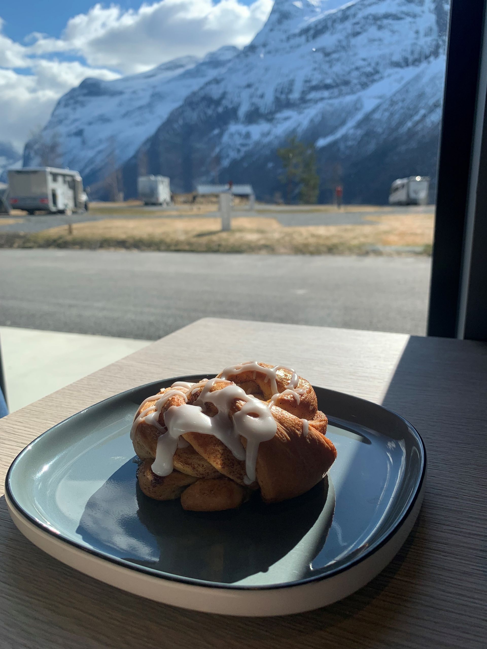 Iskald kanelbolle på en tallerken ved et vindu med snødekte fjell utenfor