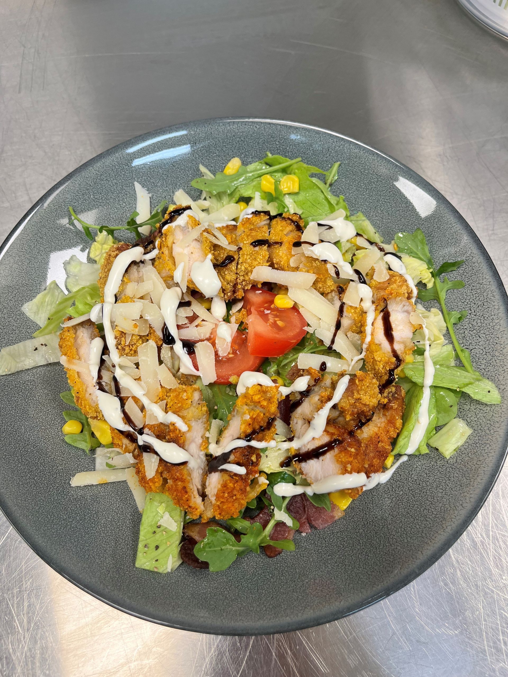 Nærbilde av en tallerkensalatbolle med grønnsaker, grillet pålegg, tomater og dryppet med hvite og mørke sauser