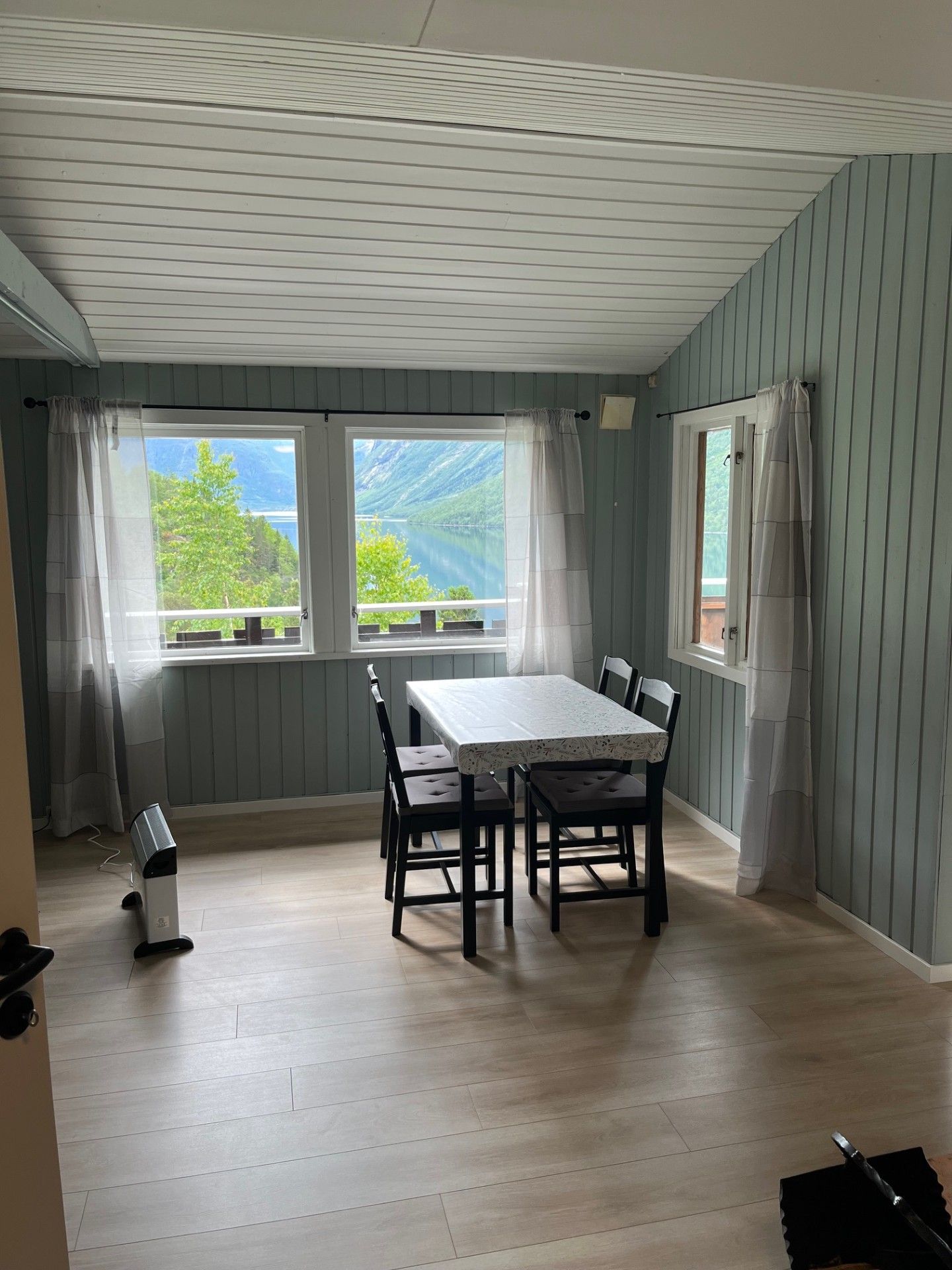 Lys spisestue med hvitt bord, svarte stoler, store vinduer og fjellutsikt