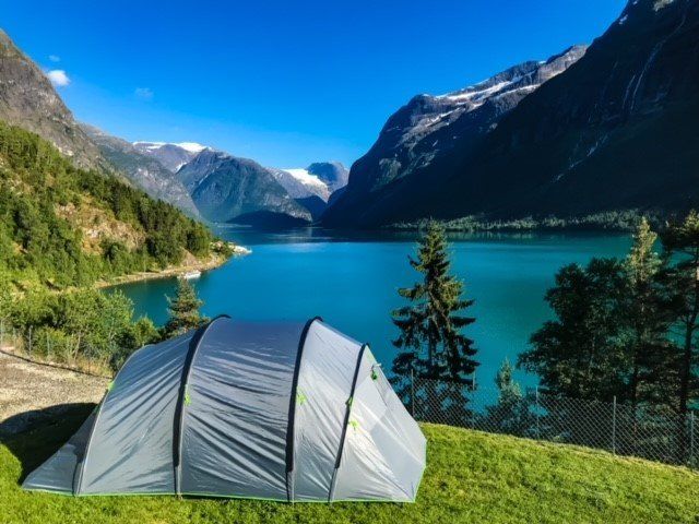 Sølvtelt ved en turkis alpin innsjø med fjell og blå himmel i bakgrunnen