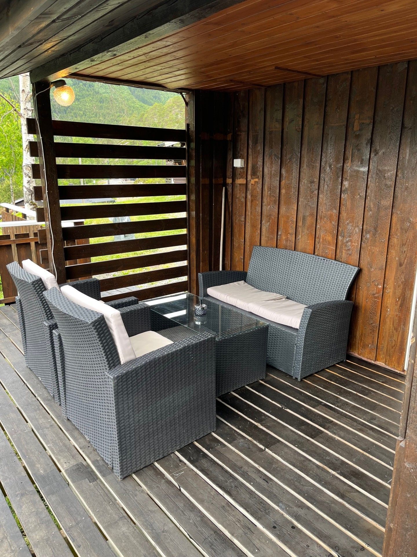 Overbygd treterrasse med sofa og stoler i mørkt rotting, stripete puter og et lite bord.