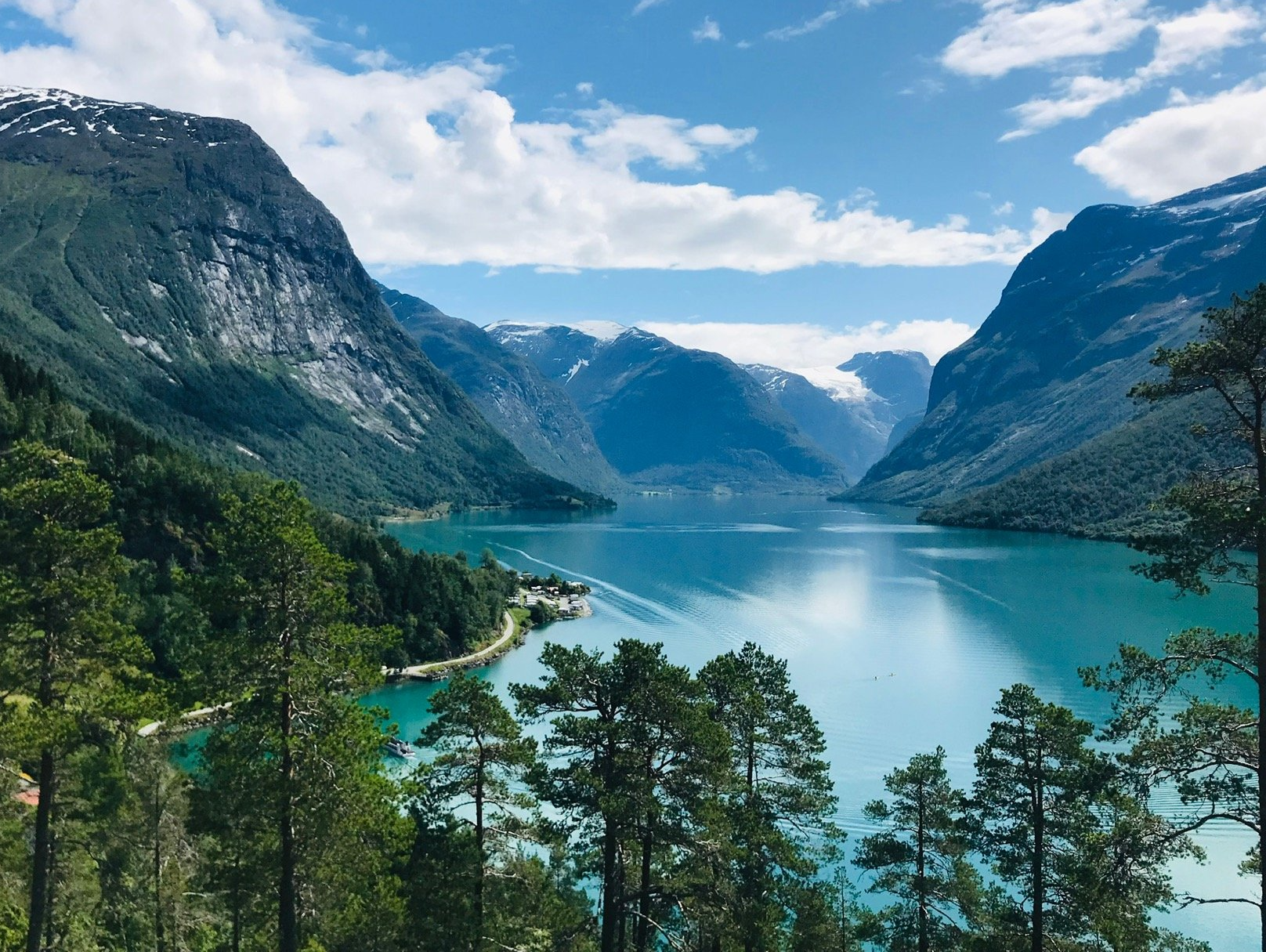 Turkis fjellsjø innrammet av furutrær og bratte, steinete topper under en blå himmel
