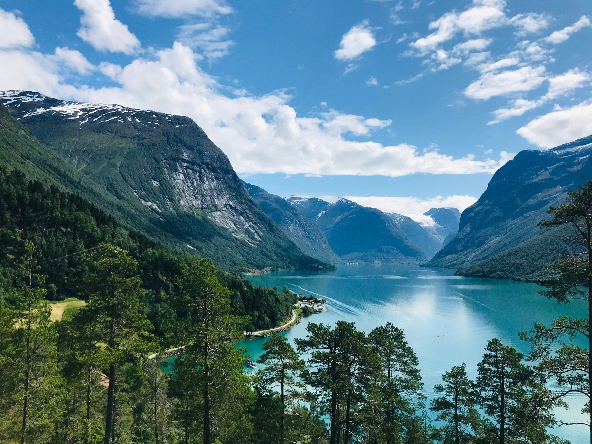 Fjellsjø mellom bratte grønne klipper under en blå himmel med skyer