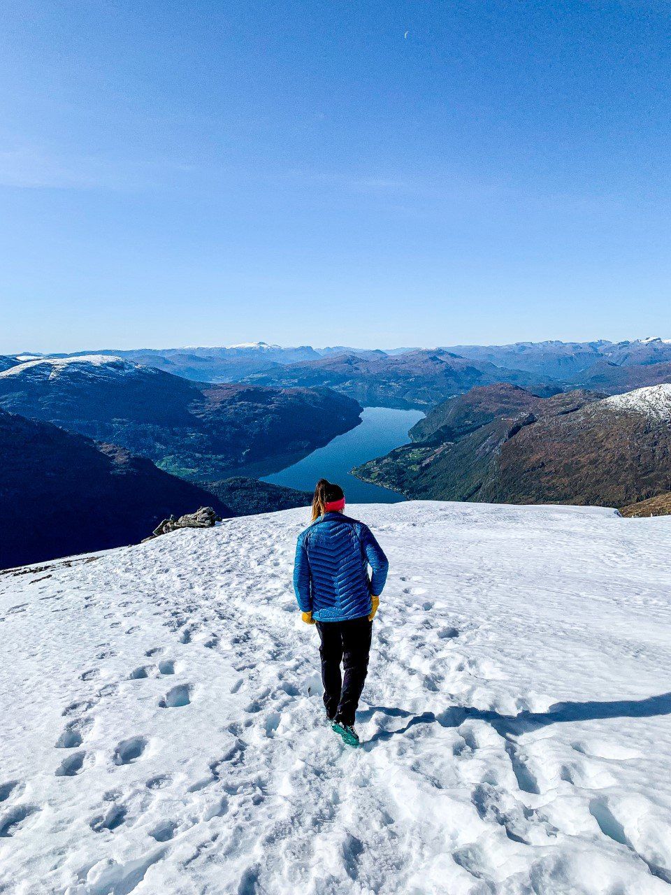 Person som står på et snødekt fjell med utsikt over blå himmel og fjerne topper