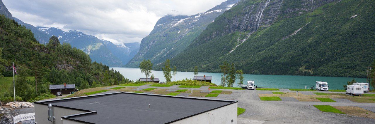Naturskjønn fjellsjø med skyer, grønn dal og noen få parkerte biler ved en vei ved vannkanten