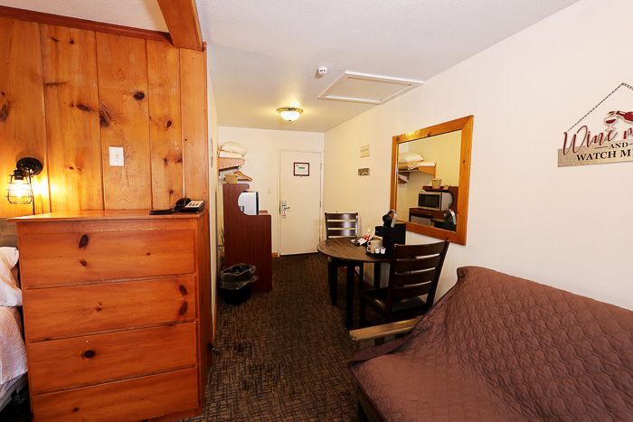 Small apartment living area with wood paneling, dining table, and brown sofa leading to a kitchen.