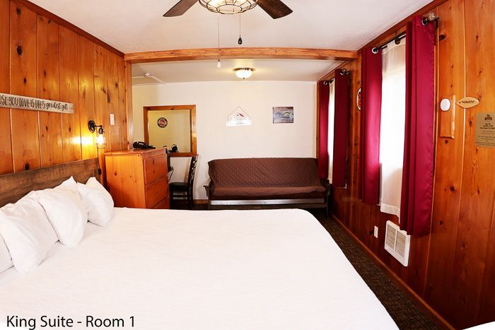 Wood-paneled king suite with bed, sofa, and red curtains in a small hotel room