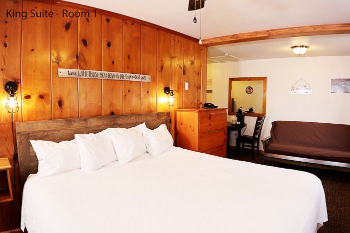 Cozy motel room with wood-paneled walls, a large bed, and a brown couch near a doorway.