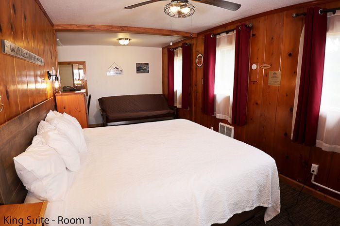 Wood-paneled king suite bedroom with white bed, sofa, and red curtains