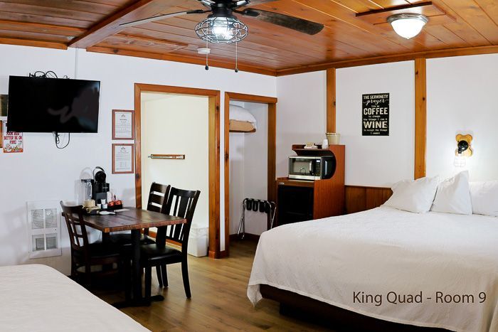 Hotel room with two beds, dining table, TV, microwave, and wooden ceiling fan