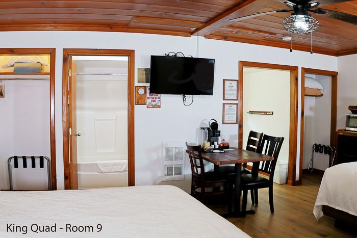 Hotel room with two beds, wall-mounted TV, wooden ceiling, and small dining table