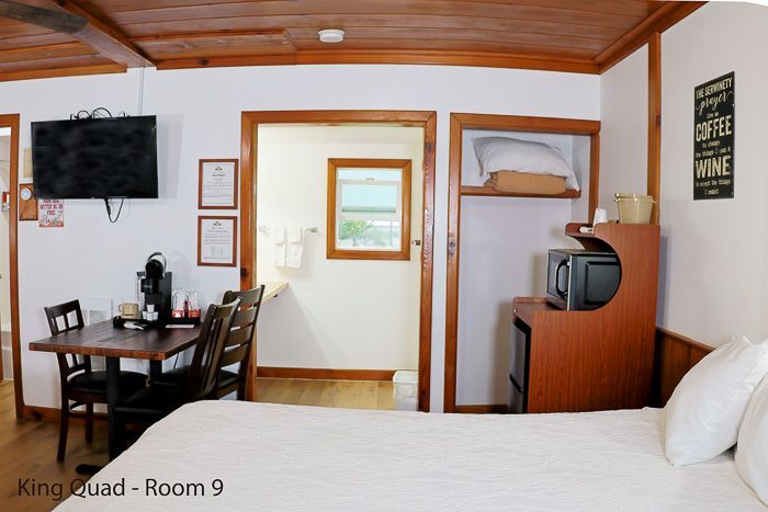 Motel room with bed, table, TV, and kitchenette, viewed toward an open doorway and bathroom area