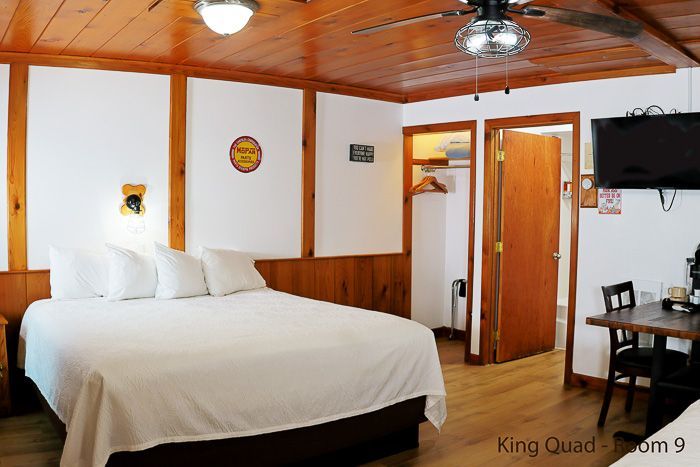 Cozy wood-paneled bedroom with a large bed, ceiling fan, and desk near a window