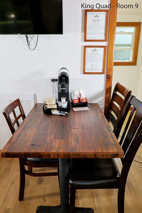 Small café table with two chairs, coffee machine, and wall menus in a room labeled “King Quad - Room 9”