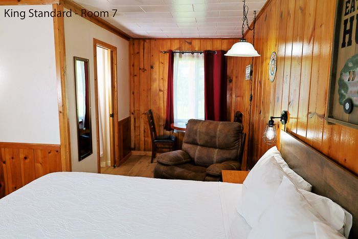 Cozy wood-paneled king standard room with bed, sofa, windows, and lamp