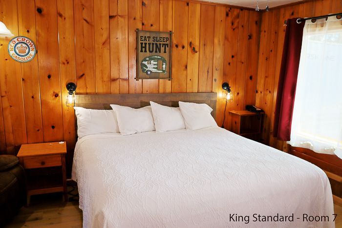 Cozy wood-paneled bedroom with a king bed, white bedding, nightstand, and bright window