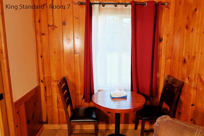 Small wood-paneled room with a round table, black chair, and a window with red curtains