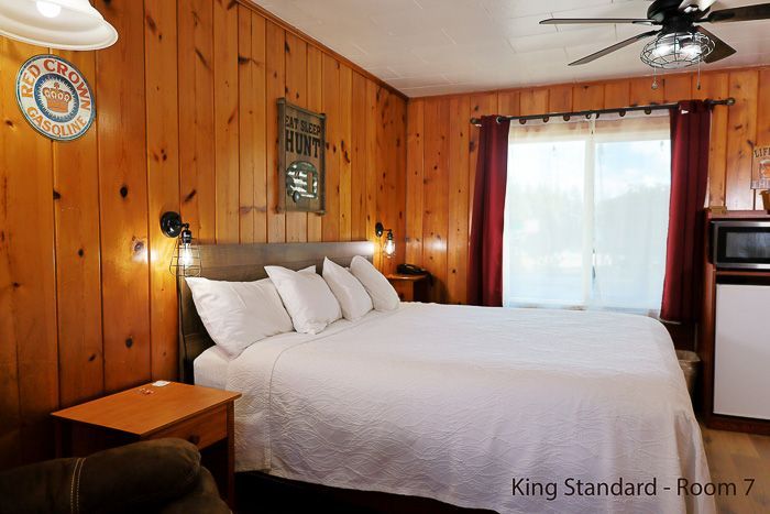 Cozy king bedroom with wood-paneled walls, white bedding, and a window with red curtains