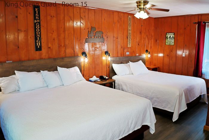 Wood-paneled hotel room with two large beds, white bedding, and warm bedside lamps