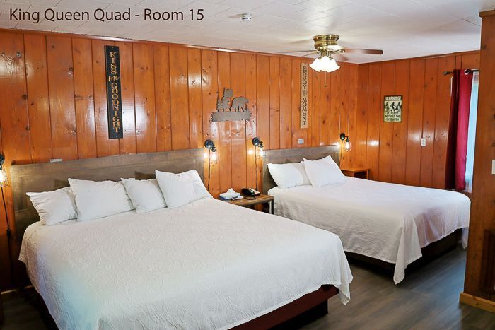 Wood-paneled hotel room with two white beds, ceiling fan, and wall lamps