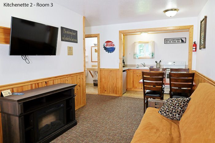 Cozy lodge common room with sofa, dining table, fireplace, wall TV, and wood-paneled trim
