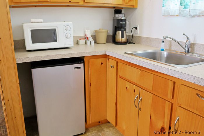 Small kitchen corner with microwave, mini fridge, coffee maker, sink, and wooden cabinets