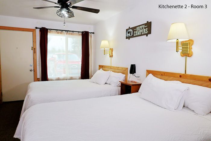 Bright hotel room with two white beds, bedside lamps, a window, ceiling fan, and wall sign
