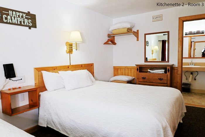 Bright hotel room with white bed, wooden furniture, lamp, mirror, and wall art