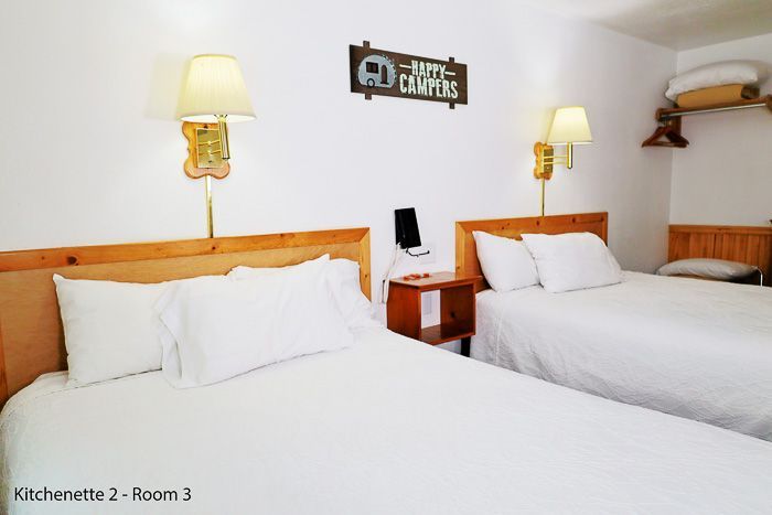 Two neatly made white beds in a bright hotel room with wooden headboards and wall lamps.