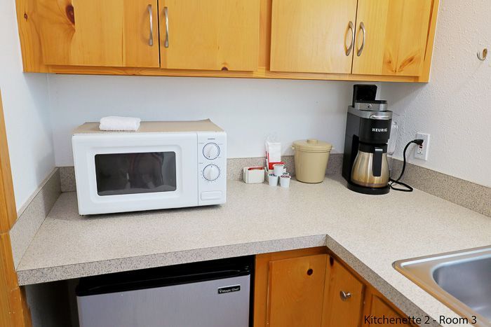 Kitchen counter with white microwave and coffee maker under wooden cabinets, next to a sink.