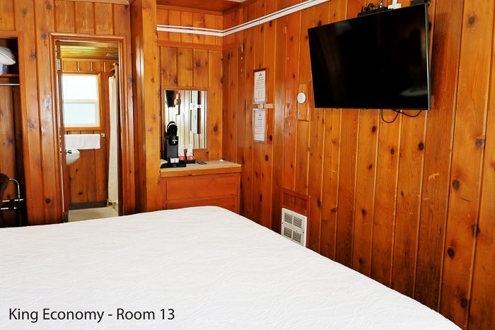 King economy hotel room with wood-paneled walls, white bed, wall mirror, and wall-mounted TV