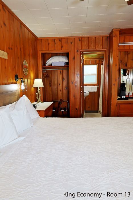 Wood-paneled king bedroom with white bed, bedside lamp, open closet, and bathroom doorway
