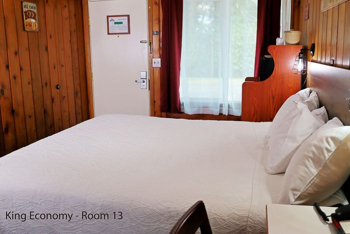 Cozy hotel room with a large bed, wood-paneled walls, and a window with sheer curtains