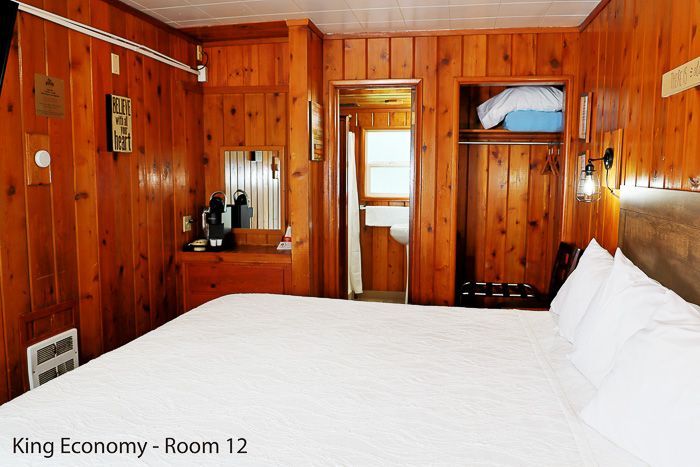 Wood-paneled hotel room with king bed, mirror, and open doorway to a bright bathroom