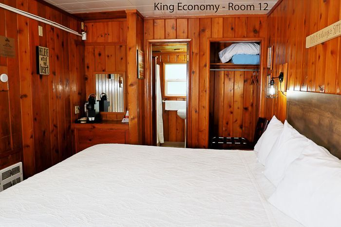 Wood-paneled hotel room with queen bed, desk, and open doorway to a bright bathroom